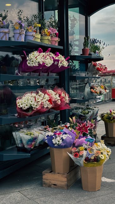 A display of floral arrangements and bouquets at a flower shop, featuring a variety of fresh flowers including white daisies, pink lilies, and purple irises, wrapped in colorful paper and decorative r