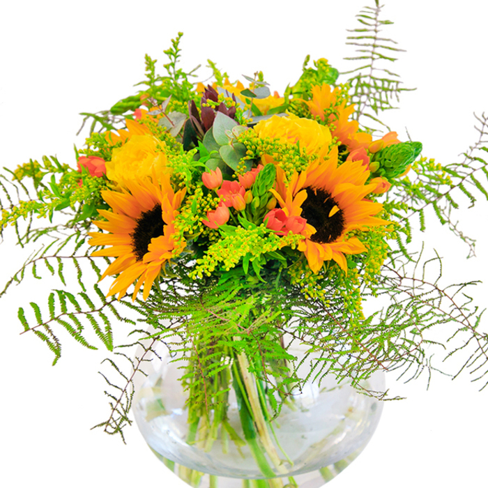 On first glance, this exuberant bouquet-artfully arranged by a seasoned Watford florist-radiates the golden brilliance of a late summer's day. The ensemble is an ode to the area's vibrant parks and gardens, where sunflowers and yellow roses bask under the sky. Generous petals of radiant sunflowers and rich, multi-layered yellow garden roses open wide, creating a dazzling display of colour and warmth. The interplay of deep green foliage, airy fillers, and feathery ferns recalls the lush borders of Woodside Playing Fields in mid-season. Clusters of glistening red hypericum berries glint amongst the greens, their polished finish a lively contrast to the matte softness of the petals. Resting in a crystal-clear, globe-like vase, the bouquet's stems form sculptural lines made even more vivid by the sparkling water. Up close, each element reveals its unique texture-the velvety drama of sunflowers, the intricate fold of rose petals, the crisp freshness of eucalyptus-while natural light lends a glowing, celebratory air. Designed to mark meaningful moments such as birthdays or anniversaries, or as a radiant centrepiece for gatherings in Watford, this arrangement embodies both beauty and heartfelt intention.