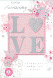 This refined anniversary card appears as a delicate blend of art and sentiment, much like the carefully balanced bouquets prepared for long-married couples across Watford. Its surface is dominated by soft, luminous tones: pearly white, misty grey, and pale powder pink flow seamlessly together, giving the design an airy, sophisticated feel, as if bathed in gentle afternoon light. At the centre lies the word LOVE, spelled out in raised capital letters with a tactile, lightly frosted texture. The edges of each letter are lined with subtle glitter, forming a fine, sparkling outline that catches the light as the card is turned in hand, reminiscent of sunlight glinting on raindrops along the Grand Union Canal. The letters sit within a blush-pink panel that glows gently against the paler background, creating a visual focal point. Around this, a spray of illustrated flowers and looping vines spreads gracefully, their delicate forms reminiscent of a florist's quick sketch before arranging fresh stems. The blossoms, in shades of powder pink, ivory, and silver-grey, are detailed with fine lines and soft shading, while tiny hints of silver foil on petals and leaves add a refined shimmer. The vines twist and curl, giving the impression of movement and lightness, as if the florals were drifting gently across the card. An elegant script message, perhaps reading On Our Anniversary and a simple phrase of enduring love, is printed in a flowing, slightly raised font that invites touch as well as sight. The overall effect is one of quiet celebration - a gentle, beautifully composed tribute to shared history, affection, and the simple joy of being together year after year in Watford.